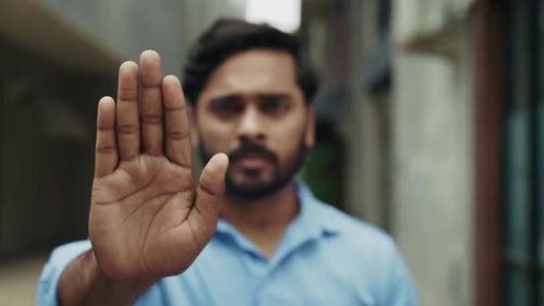 Portrait of Serious Indian Man Raises Arm Showing Stop Sign on Narrow Street