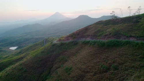 Cinematic Drone Ascend Over Hillside Road Revealing Volcano Sunrise