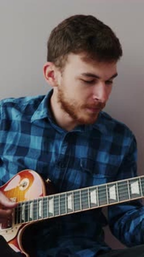 Guitarist with beard and blue shirt plays on electric guitar. Vertical video