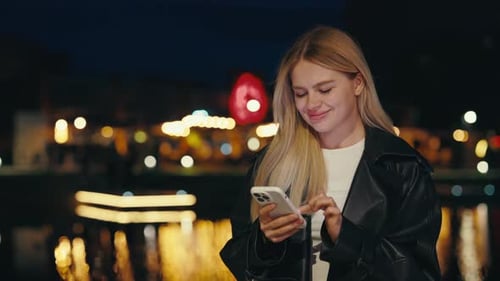 Jolie dame faisant défiler son téléphone portable debout à l'extérieur la nuit