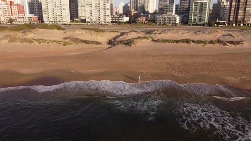 Man walking on beach at sunrise with city in background, Punta del Este in Uruguay. Aerial panoramic