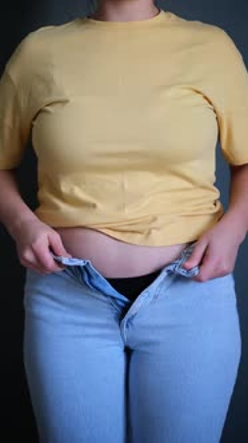 Overweight plus size woman trying to button blue small jeans