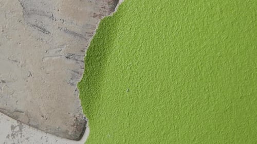steady close up shot of a man scraping off green paint from a wall