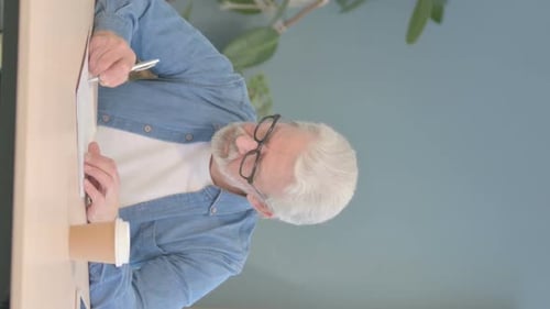 Vertical Video of Old Man Writing Letter while Sitting at Work