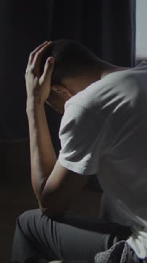 Sadness and Regret Overwhelm Young Man Sitting on Bed