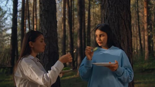 Two young women are standing with barbecue plates in summer forest