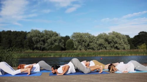 Fitness, Sport, And Healthy Lifestyle Concept - Group Of People Making Yoga Exercises On River Or...