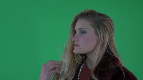 Hermosa mujer rubia con abrigo rojo posa para la cámara frente a la pantalla verde