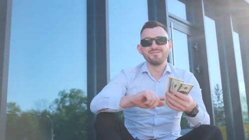 A Young Man Scatters Dollar Bills While Sitting on the Steps in Front of His Office Business People