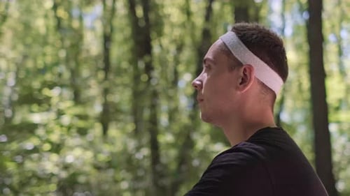 A bearded man sits in the forest on a mat, practicing meditation while listening to nature sounds.
