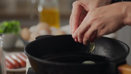 Fry. Happy young parent girl in a kitchen apron breaks an egg into a frying pan in the kitchen