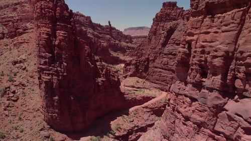 Aerial: Deep red canyon walls with narrow dirt road near Moab, Utah