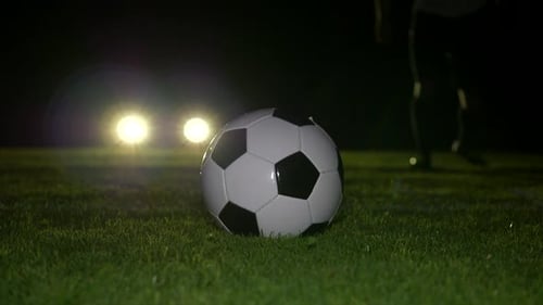 Athletic sportsman practicing soccer on football pitch at nighttime