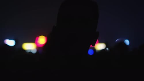 Silhouettes of people jumping, waving, taking photos or recording videos of a live music concert on