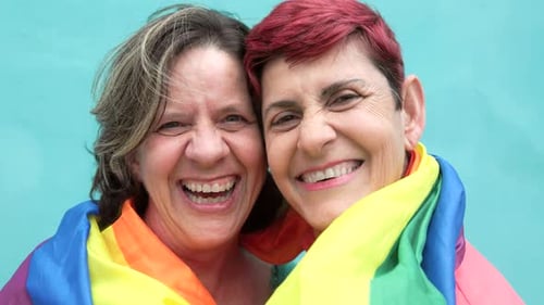Happy Senior gay lesbian couple having fun wearing Lgbtq rainbow flag at pride parade - Family love