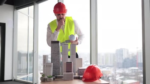 Engineer Man in Helmet and Reflective Vest Standing Near Table with Architecture Design of City