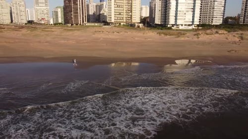 Man walking on beach at sunrise with city in background, Punta del Este in Uruguay. Aerial panoramic