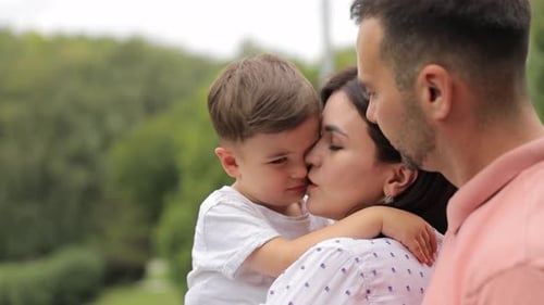 A Happy Family with a Baby Boy is Walking in the Park Together A Boy Kisses His Mother