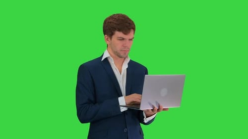 Concentrated Young Businessman Working on Laptop While Standing on a Green Screen, Chroma Key.