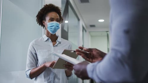 Mixed race businesswoman in face mask using digital tablet in office