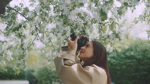 Young woman taking pictures with camera standing under a blossoming tree