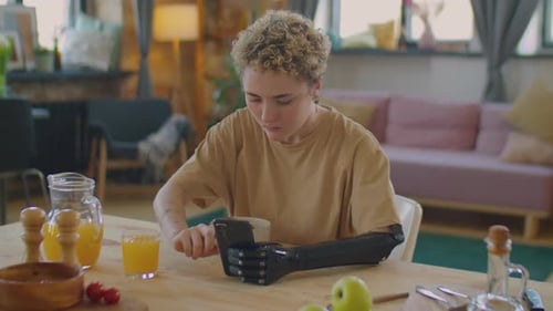 Girl with Prosthetic Arm Using Phone during Meal at Home