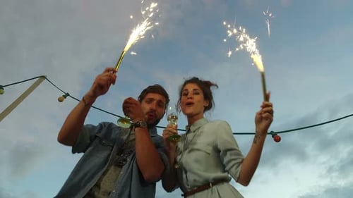 Low angle view of couple holding firework candles and toasting with champagne