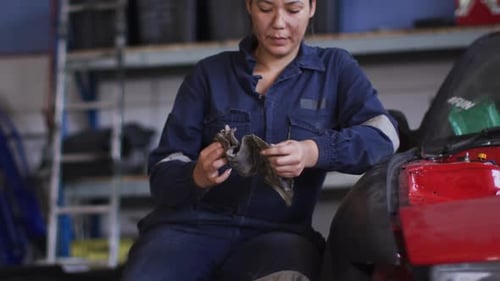 Portrait of female mechanic cleaning her hands with a cloth sitting at a car service station