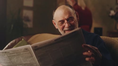 Elderly Man Sitting on Couch with Newspaper