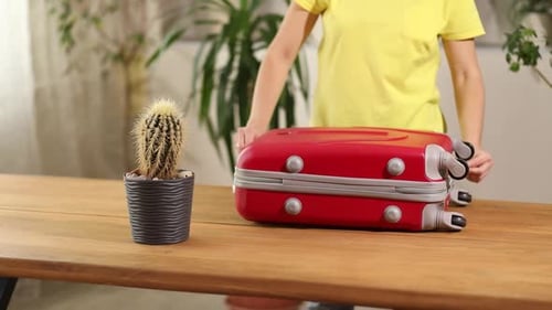 Woman close and zips red suitcase, packing, getting ready for summer vacation