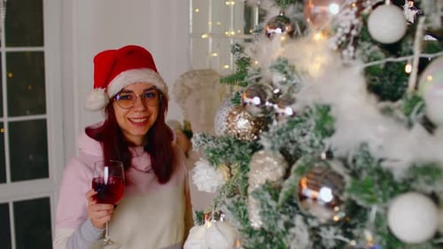 Femme rêveuse avec du vin près de l'arbre de Noël regardant au loin