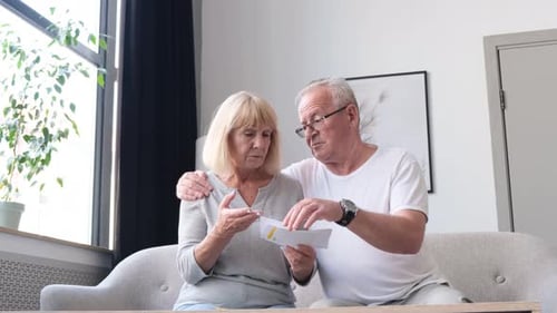 Elderly Husband and Wife Sit in White Living Room and Review Treatment Cards
