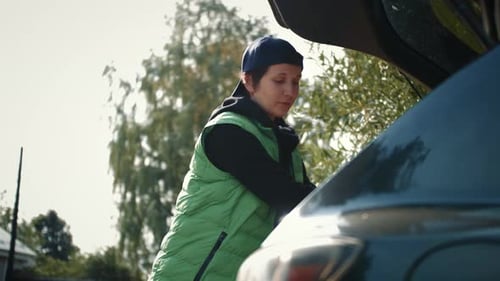 Delivery Person Putting Cardboard Boxes to Car Trunk and Using Digital Tablet
