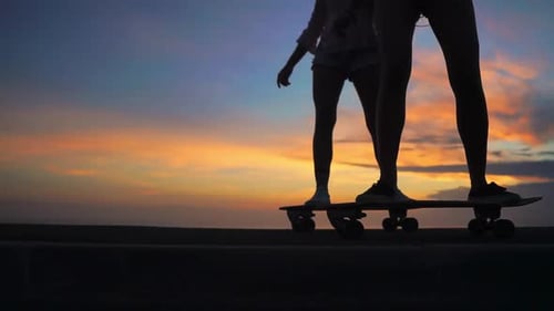 Close-up of the Legs of Two Girls Girlfriend in Shorts and Sneakers Ride Skateboards on the Slope