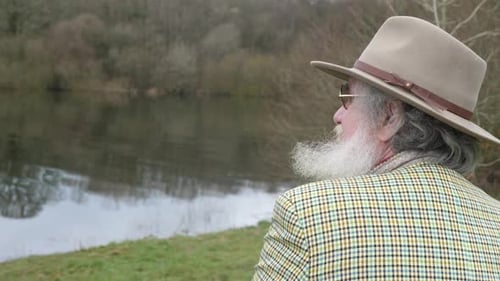 An elderly man sadly looking out over the lake
